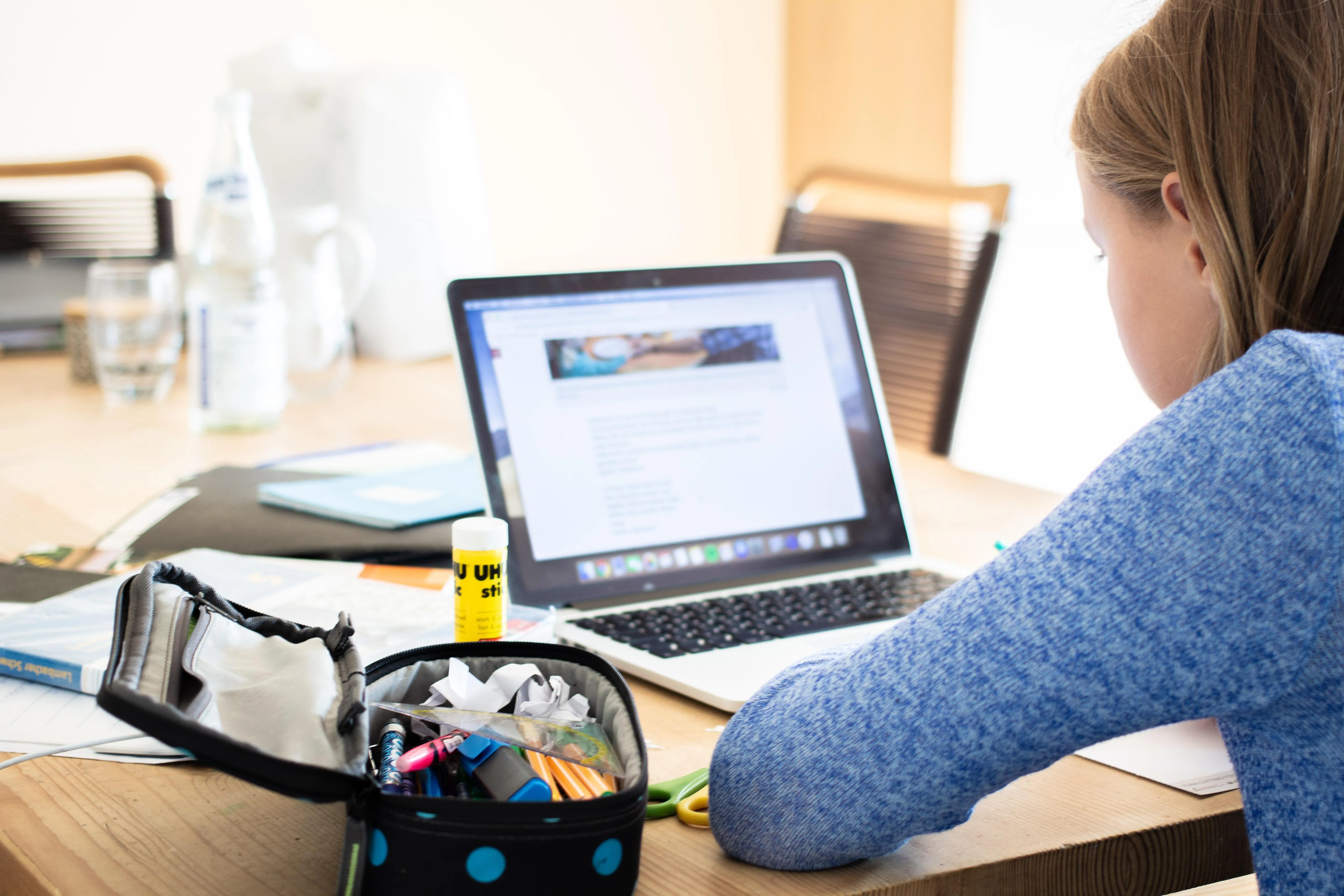 Schülerin von hinten am Laptop mit Schulmaterial, Gesicht nicht erkennbar
